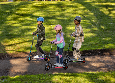 Three children on kids electric scooters in a park setting
